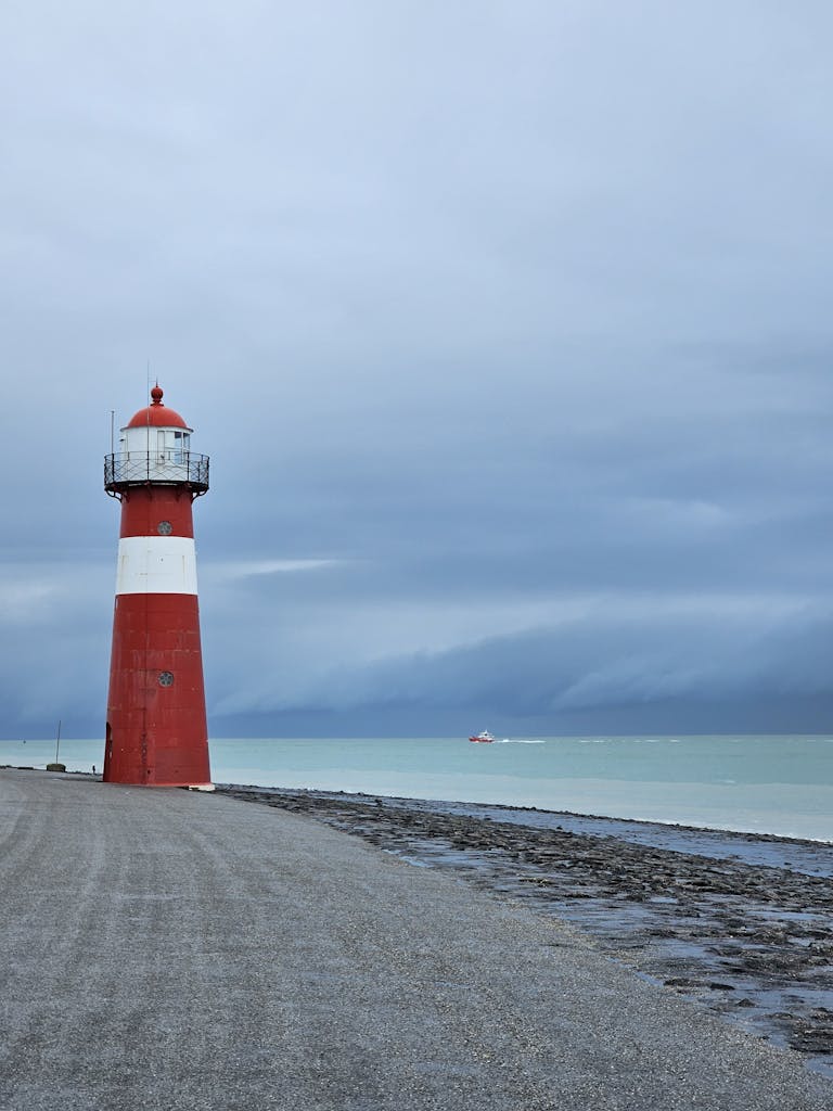 Beach by a Sea with a Lighthouse under a Cloudy Sky