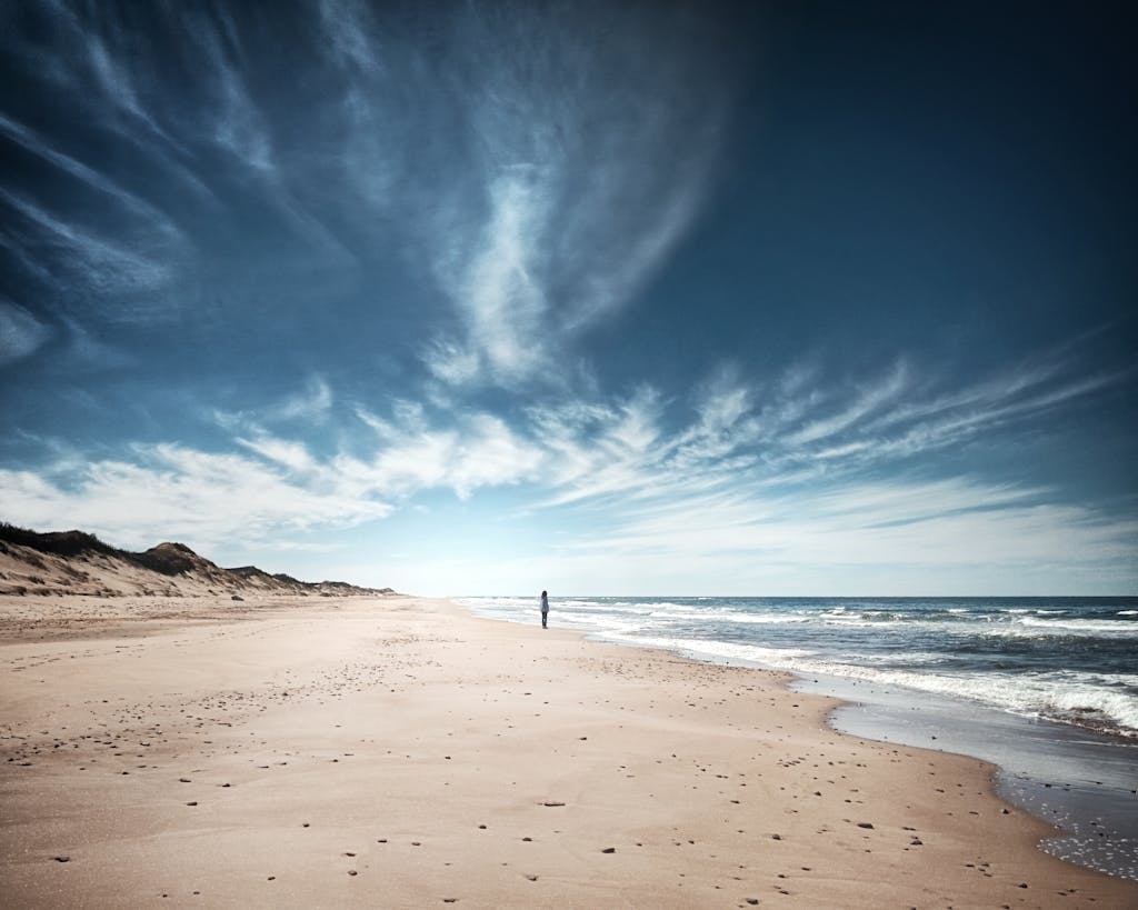 Long exposure distant person standing on sandy beach and admiring spectacular scenery of foamy waving sea under majestic blue skies