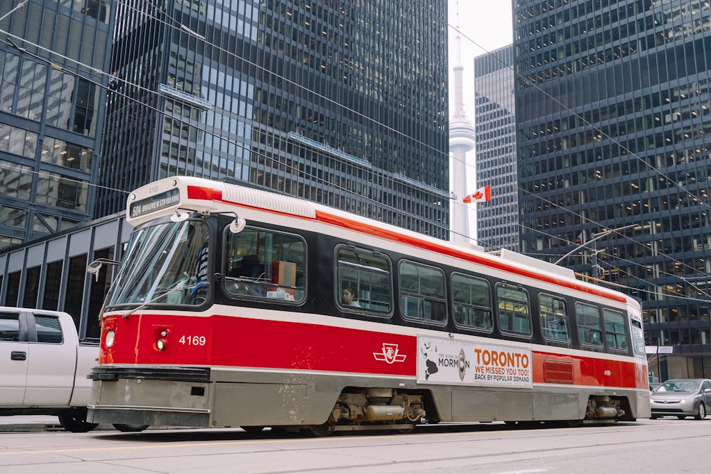 Red public tram on railroad in middle of megapolis roadway surrounded with high rise buildings